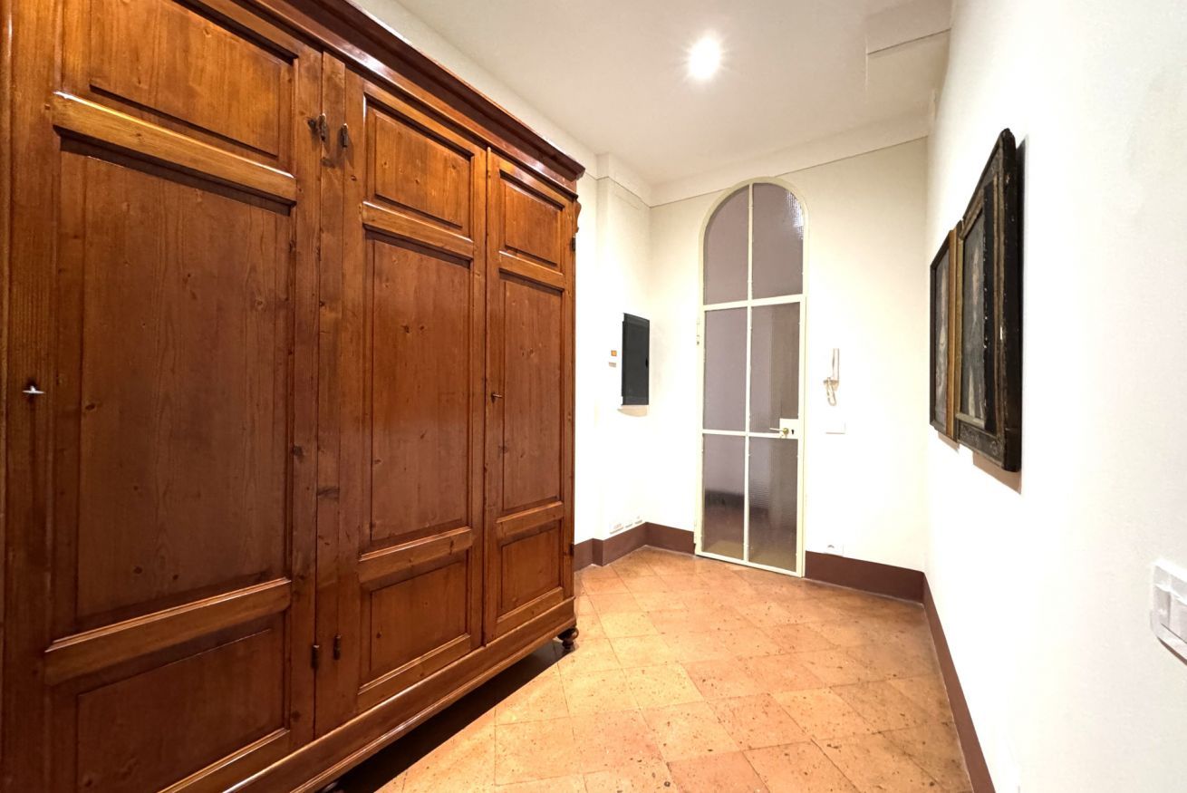 Un corridoio con porte doppie in legno, pavimento piastrellato e parete bianca con un quadro incorniciato.