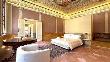 Amplia habitación de hotel con una cama grande, una mesa redonda, un sillón blanco y un techo decorativo.