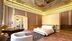 Ein geräumiges Hotelzimmer mit einem großen Bett, einem runden Tisch, einem weißen Sessel und einer dekorativen Decke.