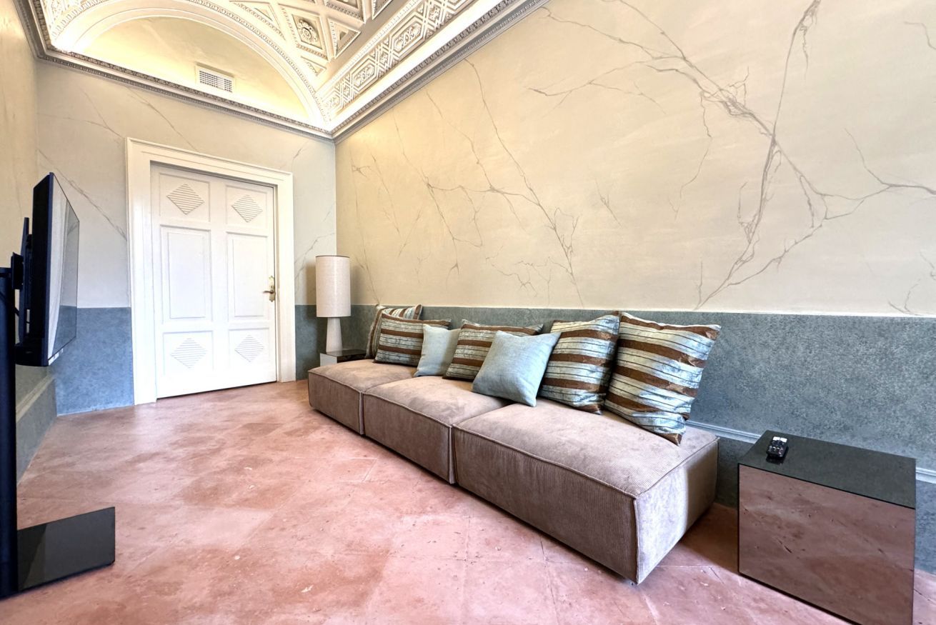 Een kamer met een beige bank, een witte deur, een marmeren muur en een kleine tafel met een lamp.