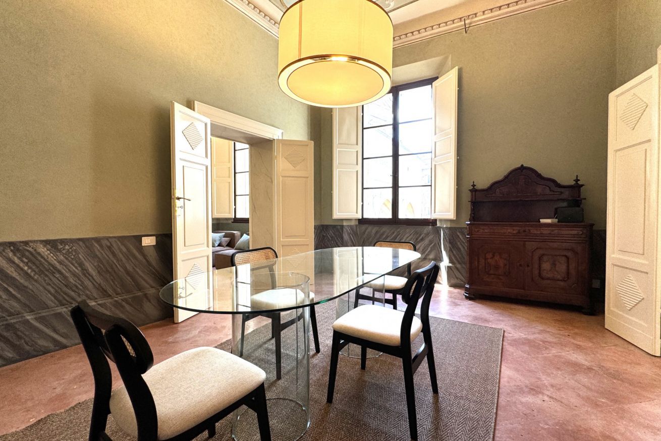 Una sala de conferencias con una mesa de cristal, cuatro sillas, un armario de madera y un amplio ventanal con contraventanas blancas.