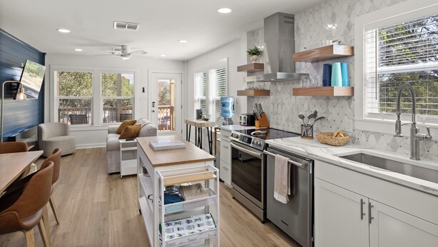 A modern kitchen with a central island, built-in oven, and a large window with blinds.