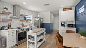 A modern kitchen with white cabinetry, a stainless steel range, and a wooden dining table with brown chairs.