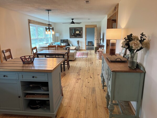 A spacious kitchen with a dining area, wooden flooring, and a view to the living room.