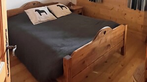 A wooden-framed bed with a dark bedspread and two pillows, a small bedside table with a lamp, and a ceiling light fixture.