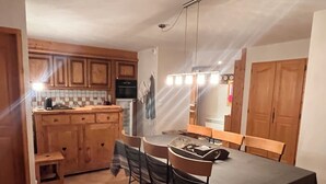 A compact kitchen with wooden cabinets, a dining table with chairs, and a small stool.