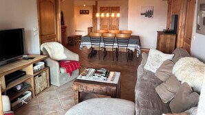 A living room with a TV, sofa, armchair, coffee table, and dining area with chairs and a table.
