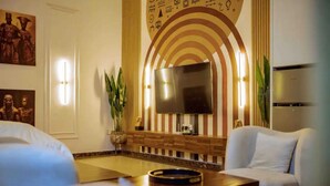 Ein modernes Wohnzimmer mit Fernseher, zwei weißen Sofas, einem Couchtisch und Zimmerpflanzen.