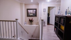 A hallway with a staircase, a framed picture on the wall, a small shelf with flowers, and a bookshelf. - 4Br Perfect 3,000 SqFt HOUSE 5st (LAS VEGAS)