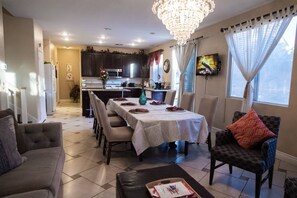 Un coin repas avec une table dressée pour quatre personnes, un lustre et un téléviseur fixé au mur.