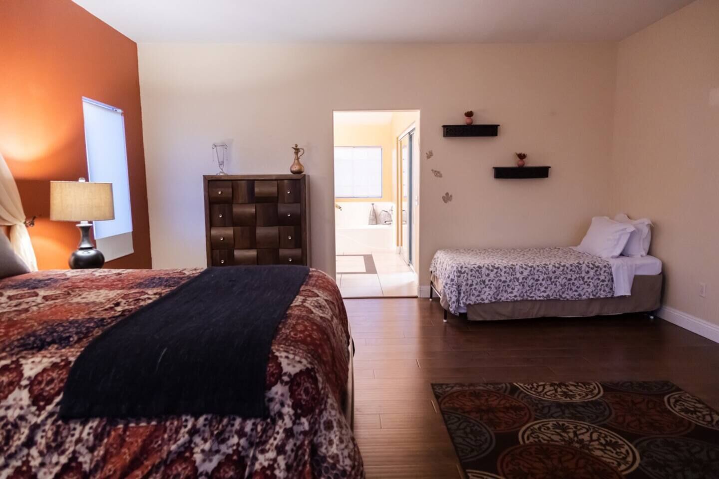 Ein Hotelzimmer mit einem großen Bett, einem kleineren Bett, einem Schminktisch, einer Lampe und Blick ins Freie.