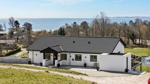 Una casa moderna con tejado de tejas, amplias ventanas y vista al mar.