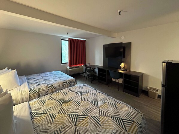 Une chambre d’hôtel avec deux lits, un bureau, une chaise, une télévision et un réfrigérateur.