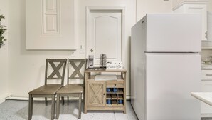 Een keuken met een witte koelkast, een koffiehoek en twee houten stoelen.