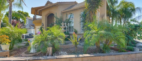 A house with a balcony, surrounded by palm trees and a small garden.