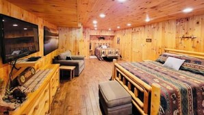A wooden cabin room with a bed, a sofa, a TV, and a small table. - Raystown Mountain Escape - Views & Relaxing Spaces (James Creek)