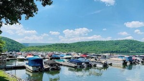 A marina with multiple boats docked, surrounded by lush green hills and a clear blue sky. - Raystown Mountain Escape - Views & Relaxing Spaces (James Creek)