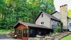 A two-story house with a stone chimney, a wooden cabin-like structure, and a stone staircase leading to the main house. - Raystown Mountain Escape - Views & Relaxing Spaces (James Creek)