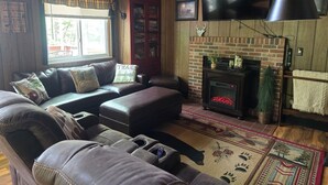 Una sala de estar acogedora con un sofá de cuero, chimenea, televisor y ventana con cortinas a cuadros.