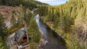 A cabin with a river, surrounded by dense forest. - Riversong Lodge by Avantstay Sauna + Hot Tub On The Truckee River (Truckee)