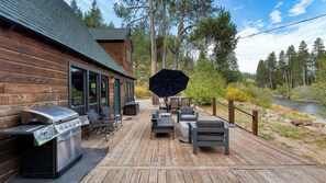 A wooden deck with outdoor furniture, a grill, and a view of a river and forest. - Riversong Lodge by Avantstay Sauna + Hot Tub On The Truckee River (Truckee)