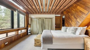 Quarto com cama grande, teto de madeira e vista para o exterior.