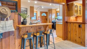 A wooden interior with a bar area, bar stools, and a kitchen visible in the background. - Riversong Lodge by Avantstay Sauna + Hot Tub On The Truckee River (Truckee)