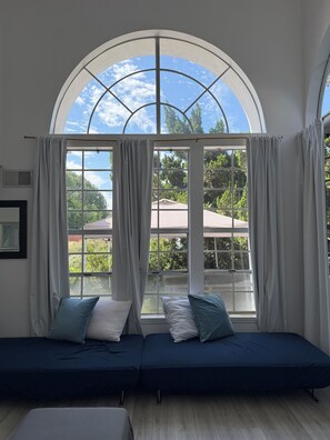 A room with a large arched window, a sofa, and a view of greenery and buildings outside.