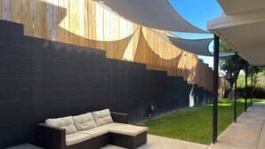Ein moderner Sitzbereich im Freien mit einer dunklen Ziegelwand, einer geschwungenen Holzkonstruktion und einer überdachten Terrasse.