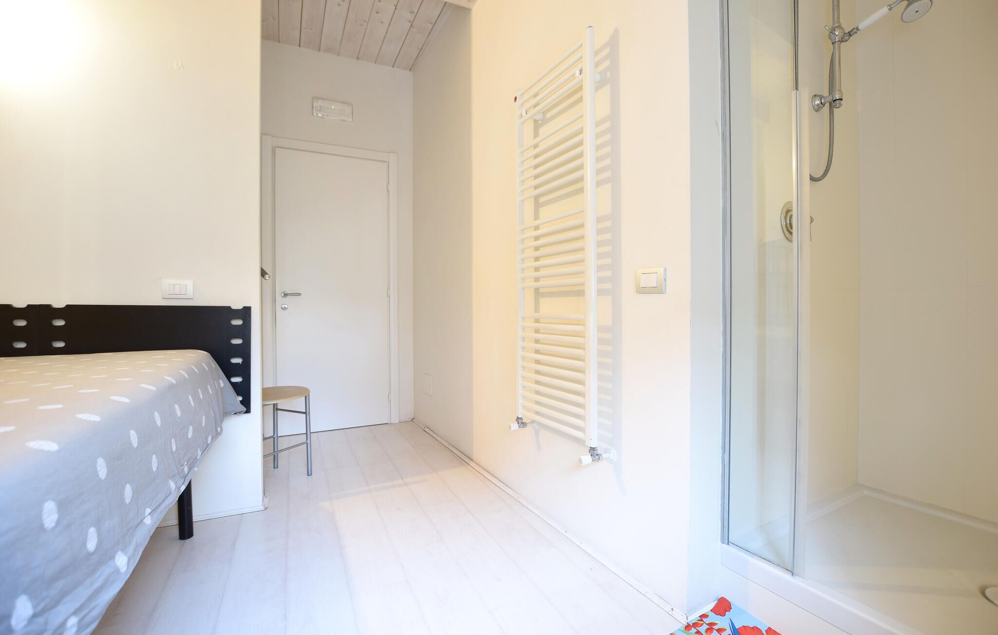 A bedroom with a bed, a chair, a radiator, and a shower area.