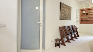 A hallway with a closed door, a bench with chairs, a small stool, and a shelf with decorative items.