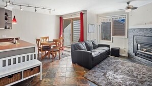 A compact living space with a dining area, a sofa, a fireplace, and a ceiling fan. - 1st floor ski in & out resort condo with hot tubs, fitness room, covered garage. (Winter Park)