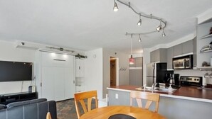 A modern kitchen with a central island, a dining area with a round table, and a living area with a sofa and TV. - 1st floor ski in & out resort condo with hot tubs, fitness room, covered garage. (Winter Park)