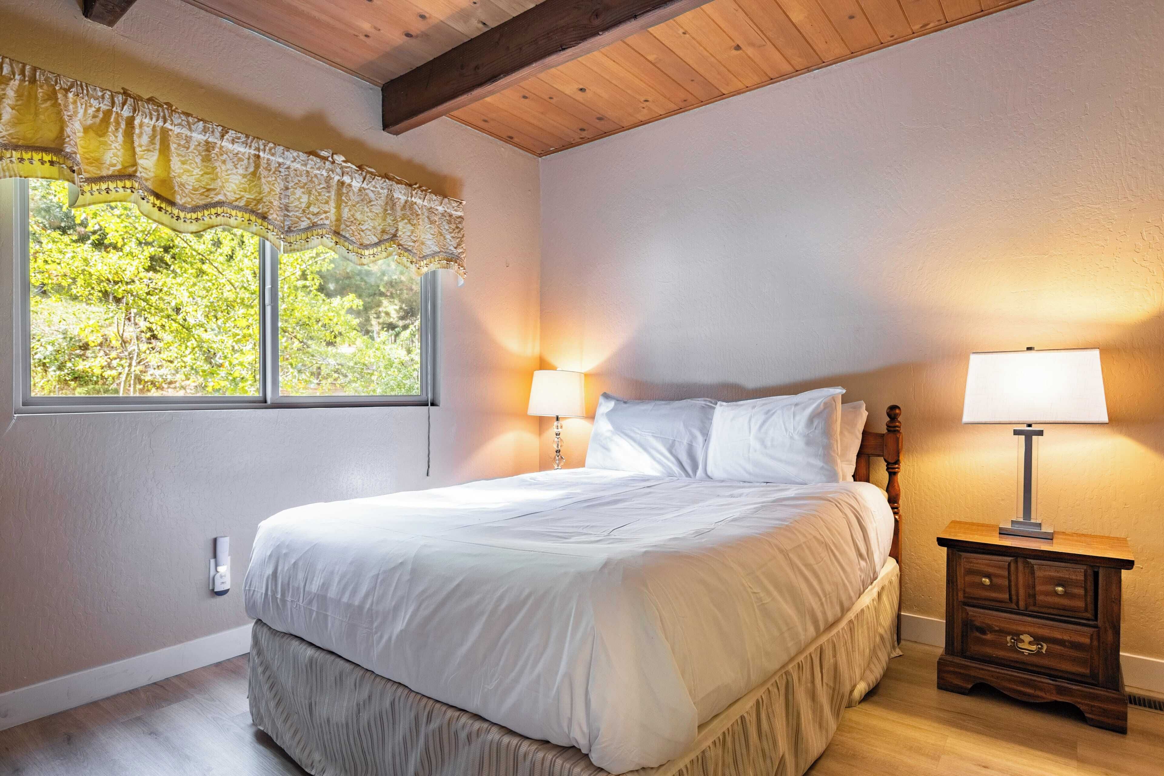 Un dormitorio con una cama grande, dos lámparas de noche, un ventanal con encaje y una mesita de noche de madera.