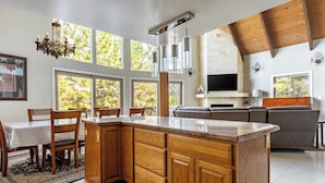 A modern kitchen with wooden cabinets, a large island, and a dining area with chairs and a table. - Mystic Ridge by Avantstay Game Room + Views (Lake Arrowhead)