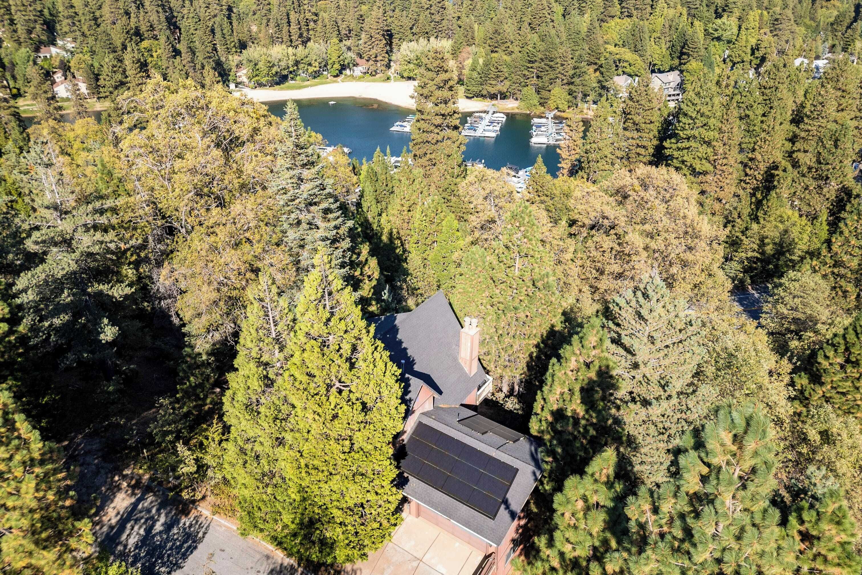 An aerial view of a house surrounded by dense forest, with a dock and boats visible in the background.