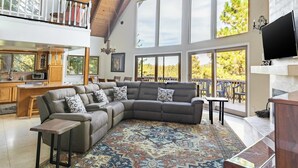 A spacious living area with a large sectional sofa, a dining table, and a kitchen in the background. - Mystic Ridge by Avantstay Game Room + Views (Lake Arrowhead)