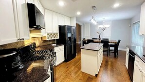 Una cocina moderna con armarios blancos, un refrigerador negro, una estufa y un comedor con candelabro.