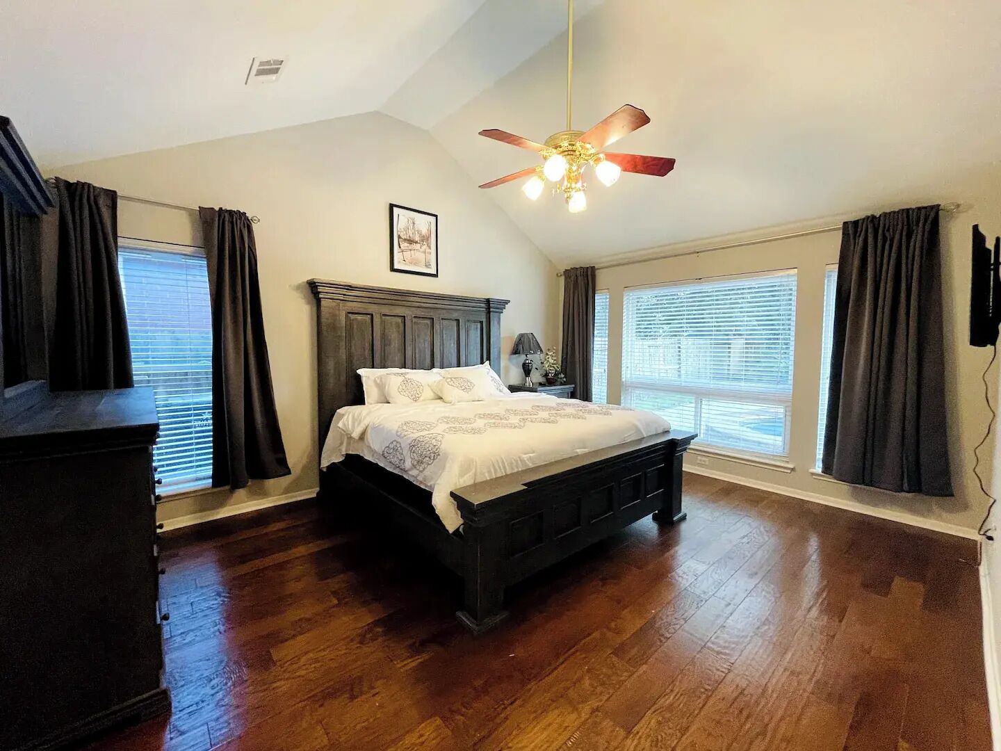 Une chambre à coucher avec un lit en bois, un ventilateur de plafond et de grandes fenêtres avec des rideaux.