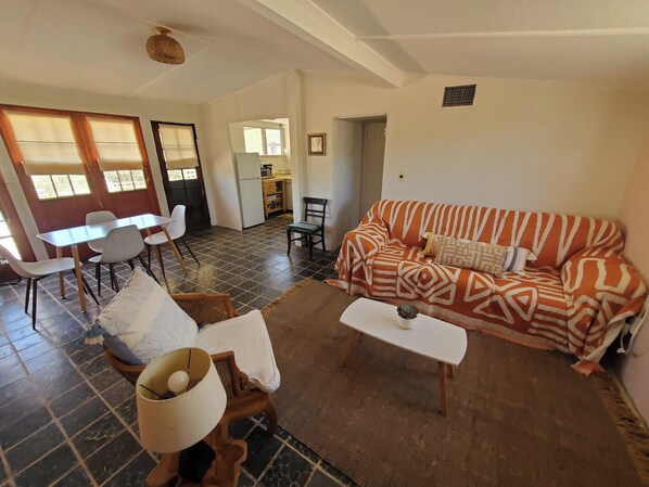 A living room with a sofa, coffee table, and chairs. There is a kitchen area in the background.