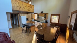 Una cocina amplia con gabinetes de madera, un comedor con una mesa grande y sillas, y vista al exterior por una ventana.