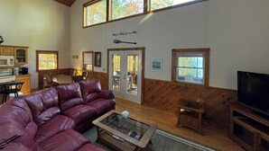 Amplia sala de estar con sofá de cuero, una mesa de centro y un televisor. Varios ventanales ofrecen luz natural y vistas al exterior.