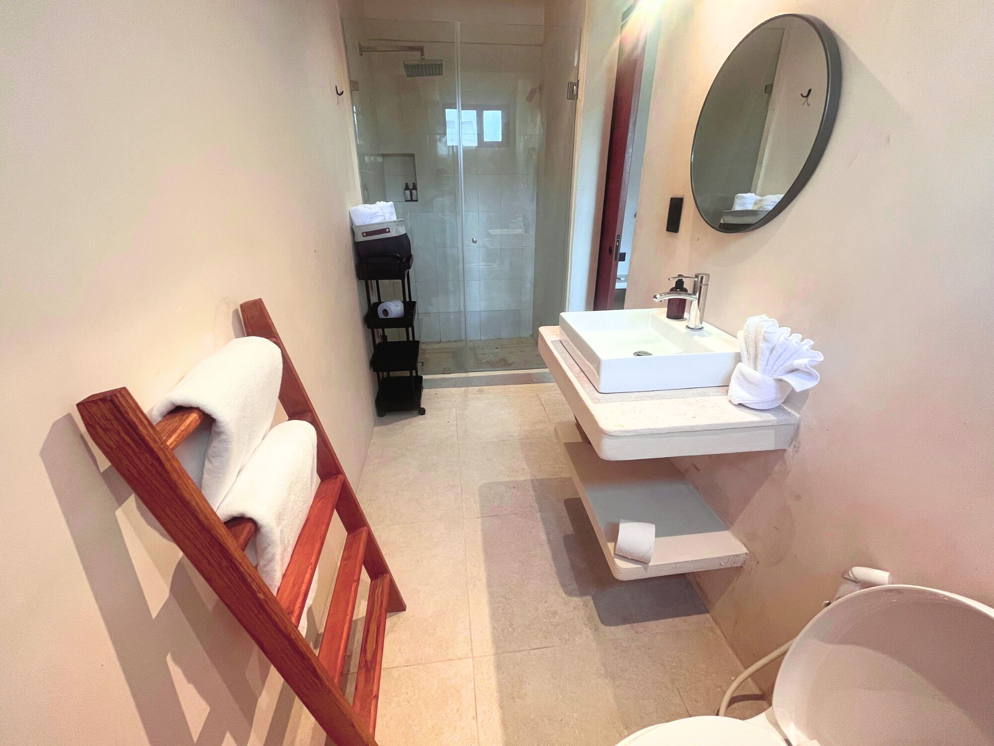 A bathroom with a wooden bench, a sink with a mirror, and a shower area.