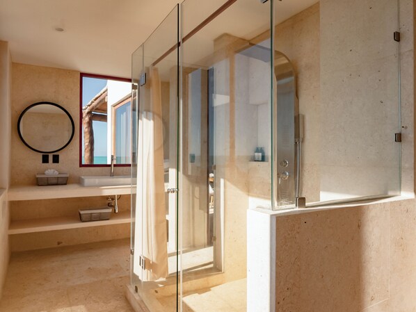 A modern bathroom with a glass-enclosed shower, a round mirror, and a built-in sink. - Beachfront Hotel Boutique DK (Isla Holbox)