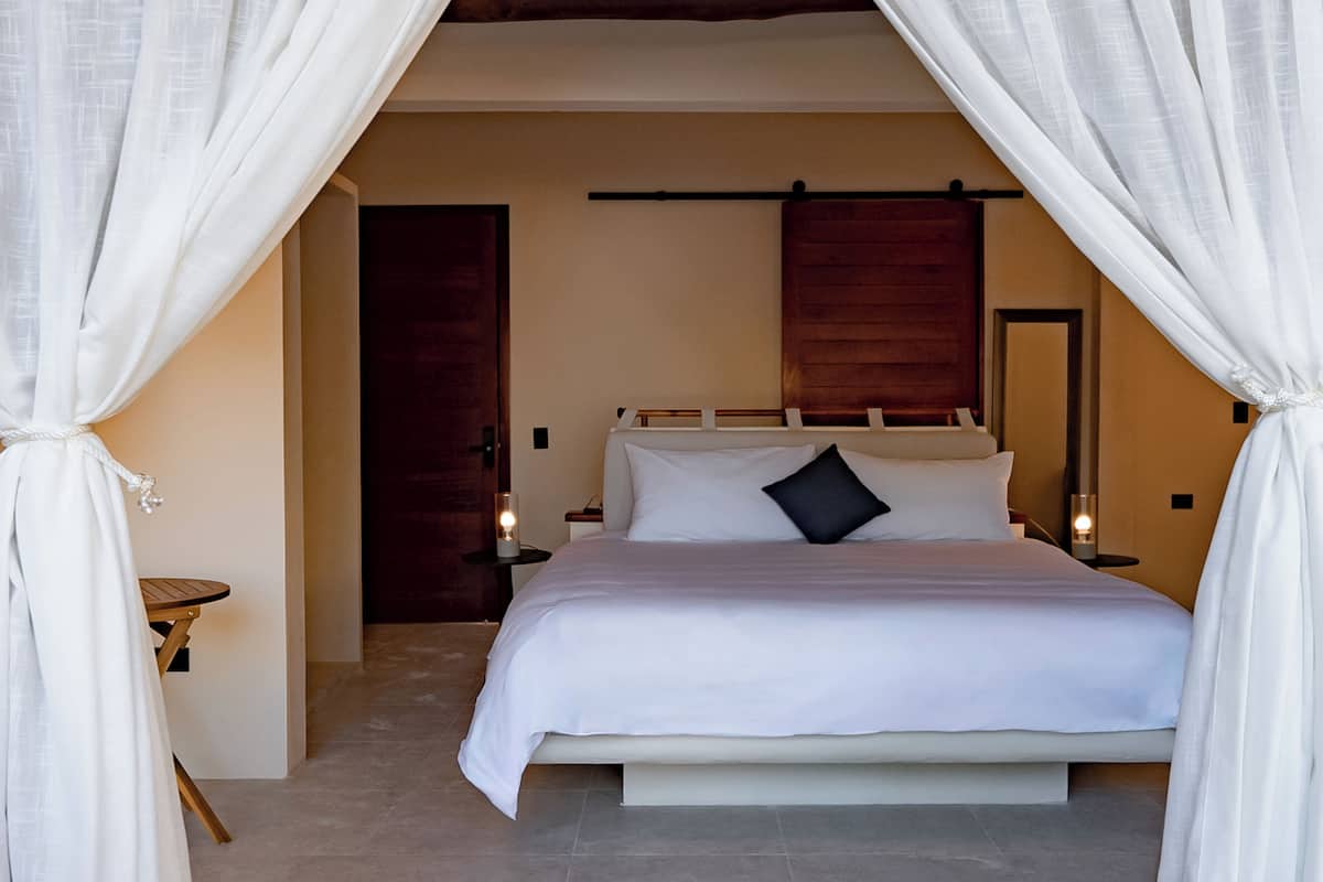 Quarto com cama, cortinas, mesas de cabeceira e cabeceira de madeira.