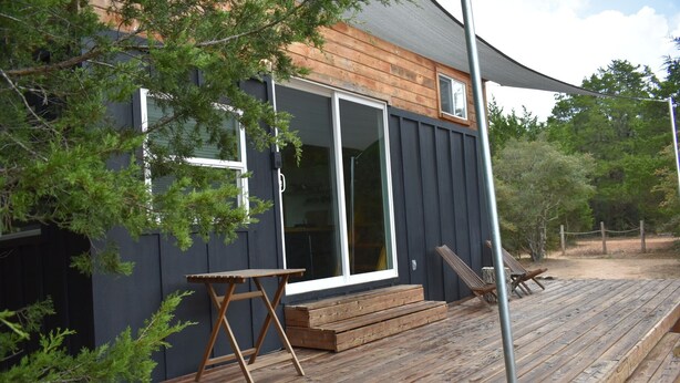 A wooden deck with a table and chairs, a sliding glass door, and a small porch area. - Secluded Tiny Home, firepit stargaze hike pond (Paige)