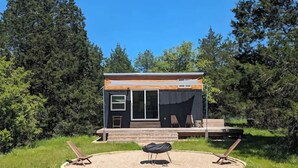 A modern cabin with a deck, surrounded by a circular seating area with two chairs and a grill. - Secluded Tiny Home, firepit stargaze hike pond (Paige)