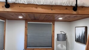 A cozy room with a bunk bed, a sofa with cushions, a small table, and a window with blinds. - Secluded Tiny Home, firepit stargaze hike pond (Paige)