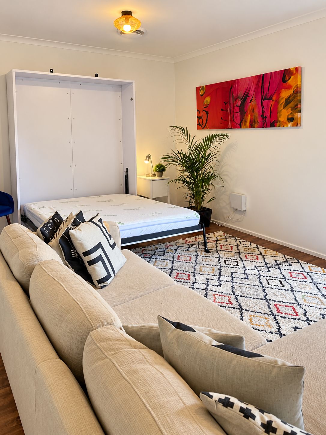 A minimalist living room with a sofa, a bed, a plant, and a colorful abstract painting.