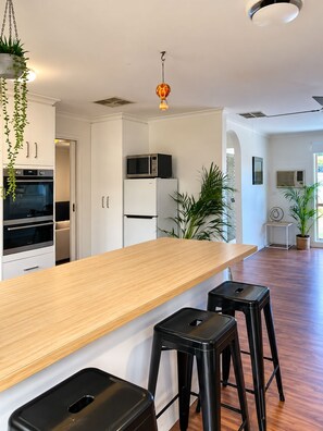 A modern kitchen with white cabinetry, a wooden countertop, and black stools. - Berwick Tweed - Peace and comfort (Melbourne)